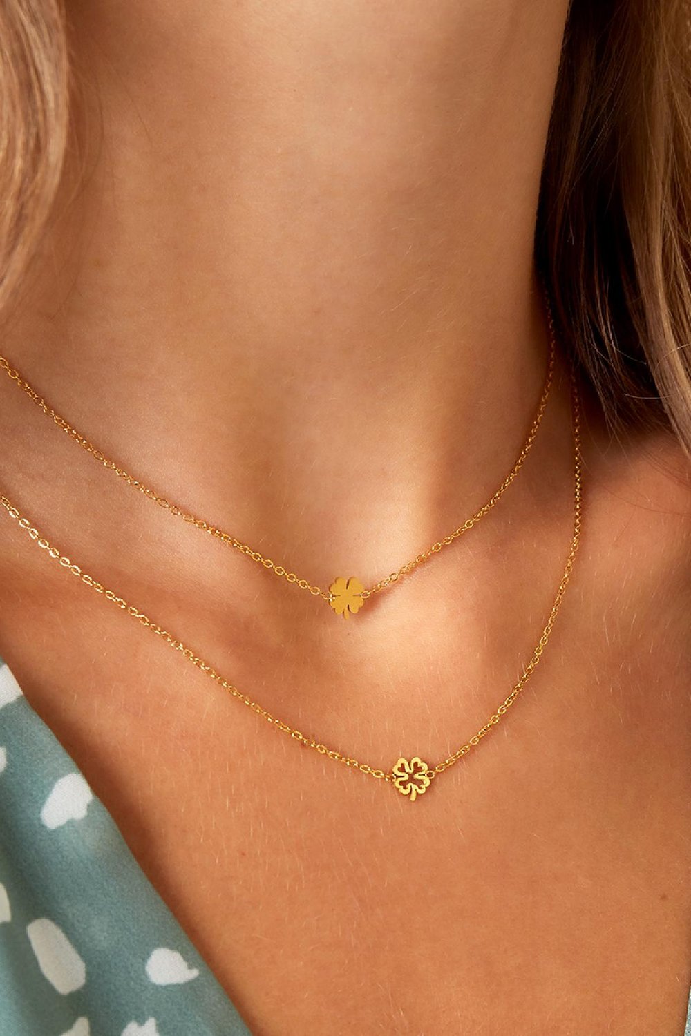 Gold-toned layered necklace featuring two dainty chains with small four-leaf clover charms on a model.