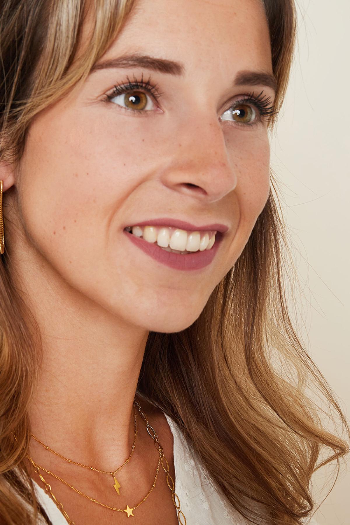 Smiling woman wearing the delicate gold lightning bolt necklace layered with other fine gold necklaces