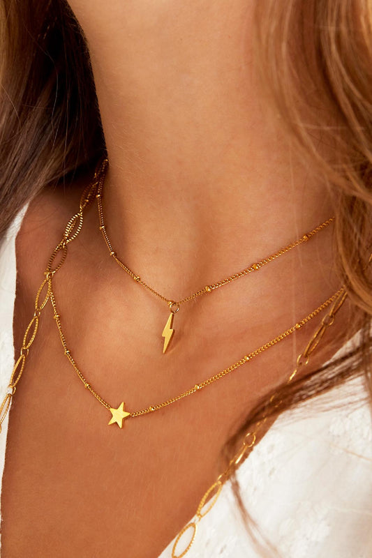 Close-up of layered necklaces on woman's neck including the gold lightning bolt necklace paired with a star pendant and chain links