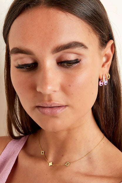Model wearing gold-tone clover charm necklace paired with pastel pink top and matching earrings