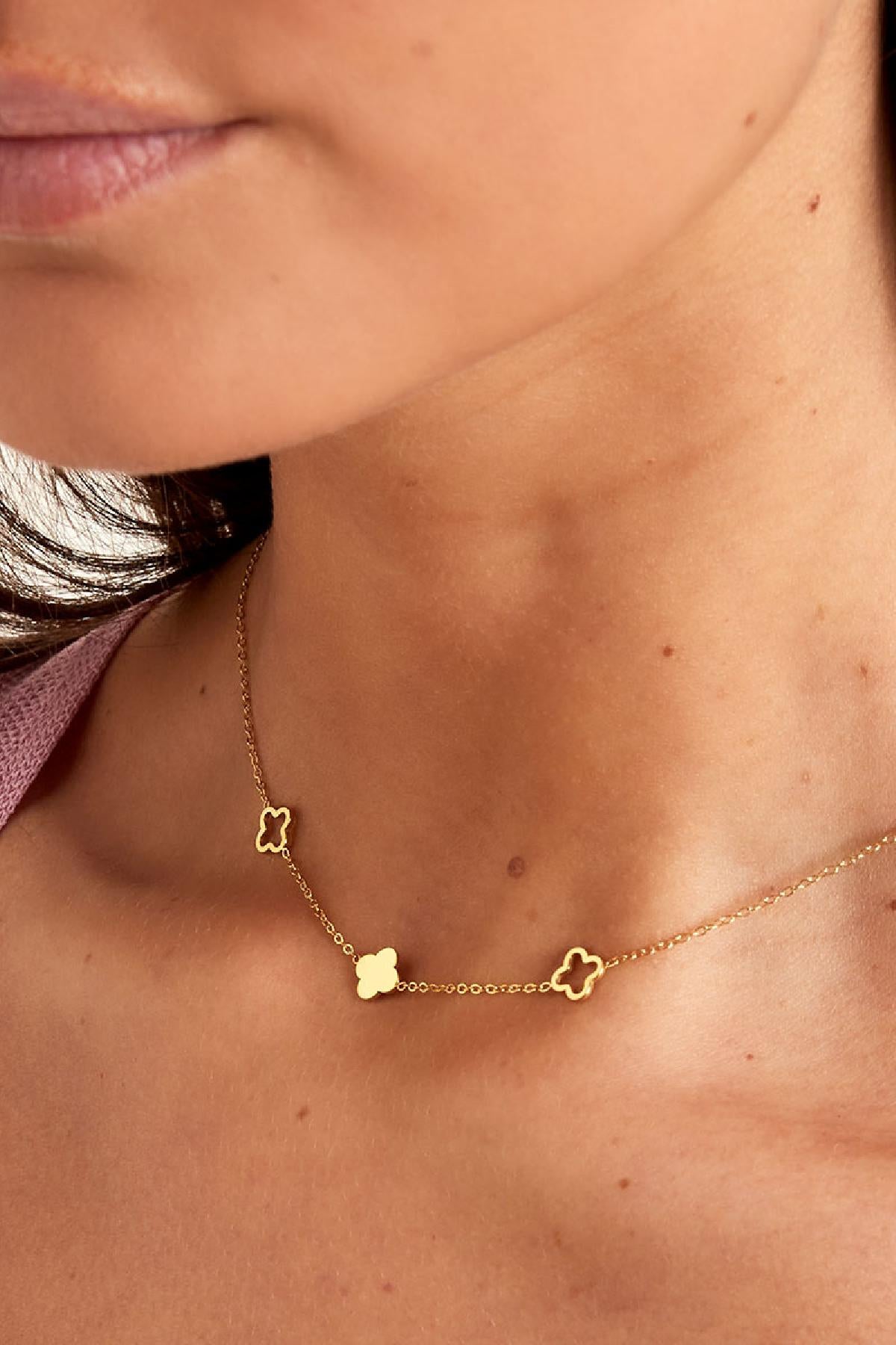 Close-up of the gold-tone necklace's clover charms resting on model's collarbone