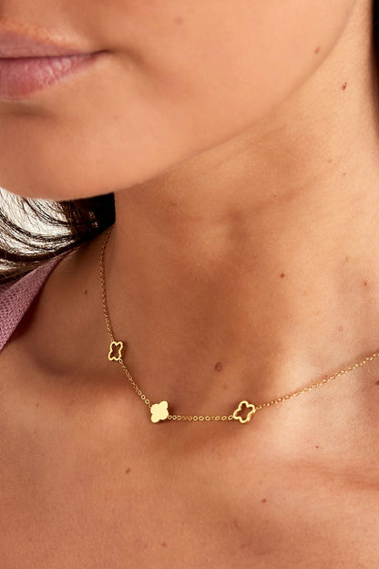 Close-up of the gold-tone necklace's clover charms resting on model's collarbone