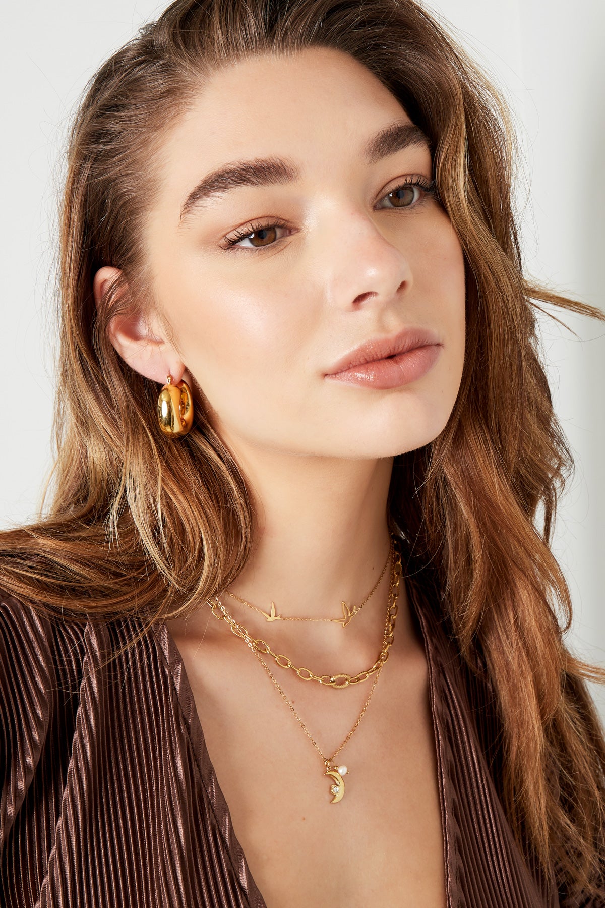 Woman wearing layered gold necklaces including the bird charm necklace paired with chunky gold hoop earrings