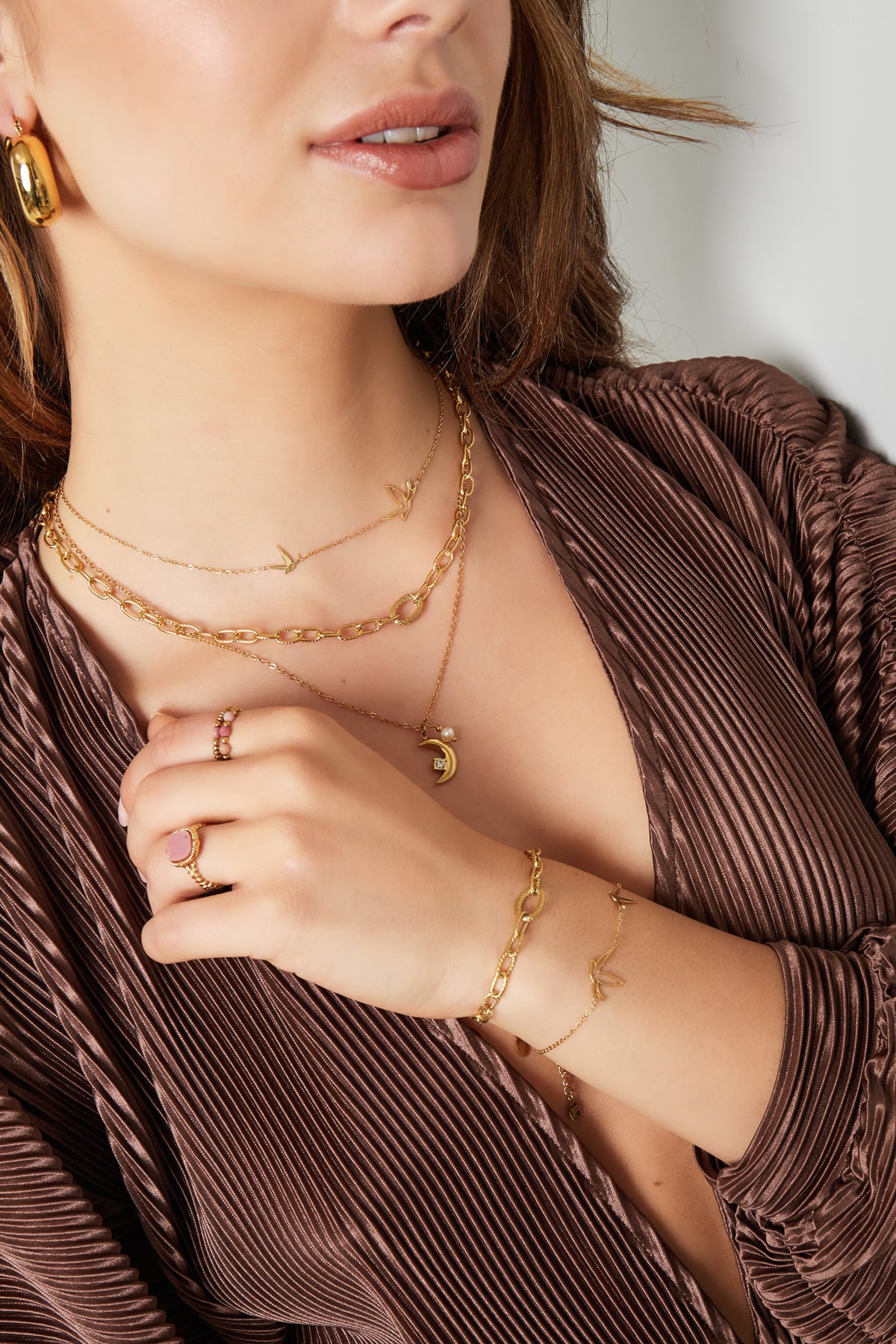 Woman styled in a brown top wearing the gold bird charm necklace along with matching gold chain bracelet and rings