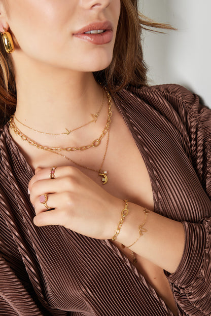 Woman styled in a brown top wearing the gold bird charm necklace along with matching gold chain bracelet and rings