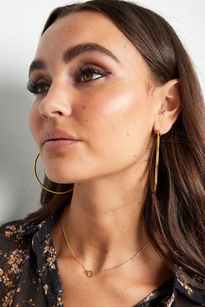 Model wearing delicate gold linked circle necklace paired with large gold hoop earrings and floral blouse