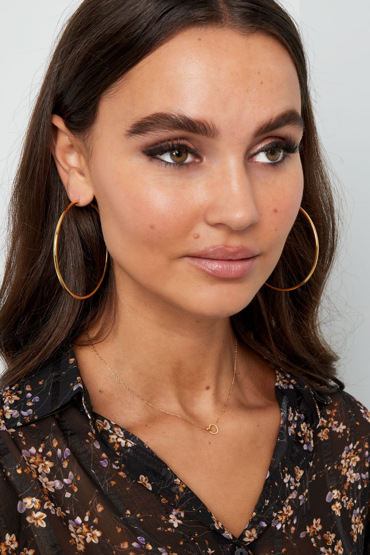 Model wearing the delicate gold linked circle necklace and large hoop earrings, styled with floral black blouse