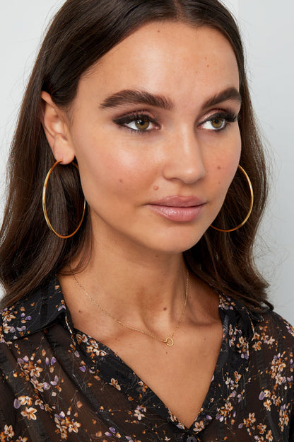 Model wearing the delicate gold linked circle necklace and large hoop earrings, styled with floral black blouse