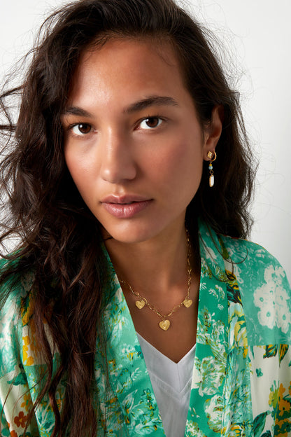 Model showcasing the gold triple heart necklace paired with a green floral top