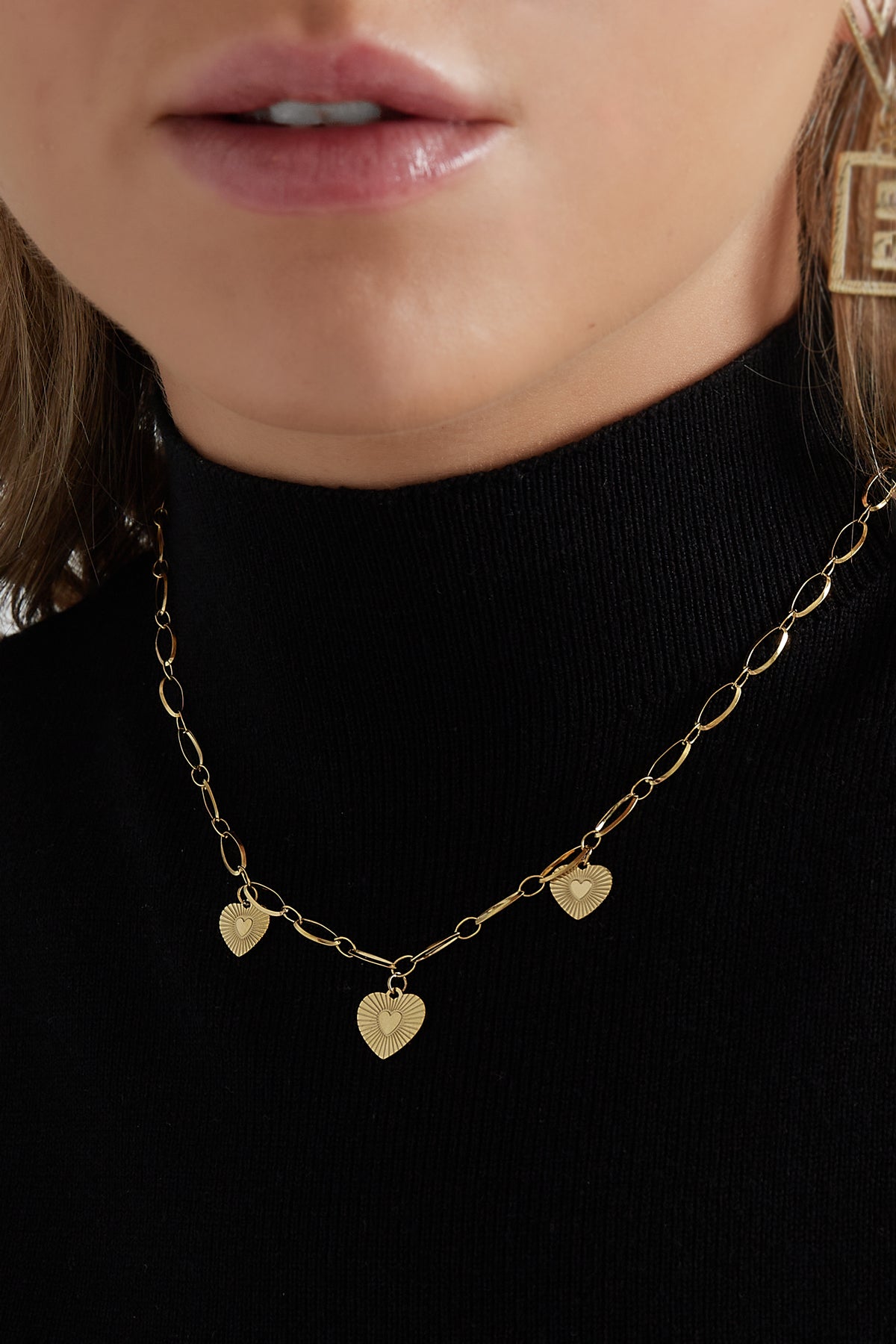 Close-up of model wearing the gold triple heart necklace over a black turtleneck