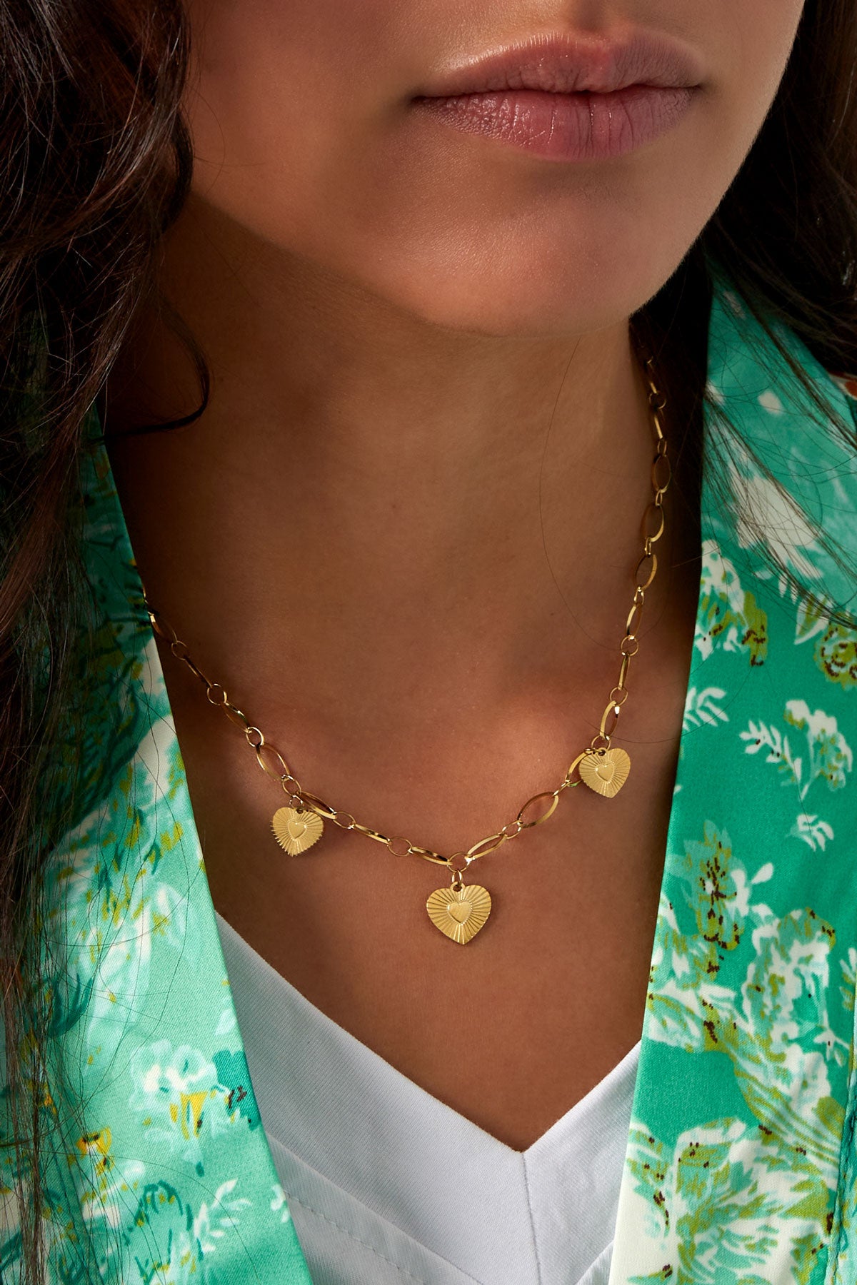 Close-up of necklace featuring three gold hearts with sunburst pattern on linked chain