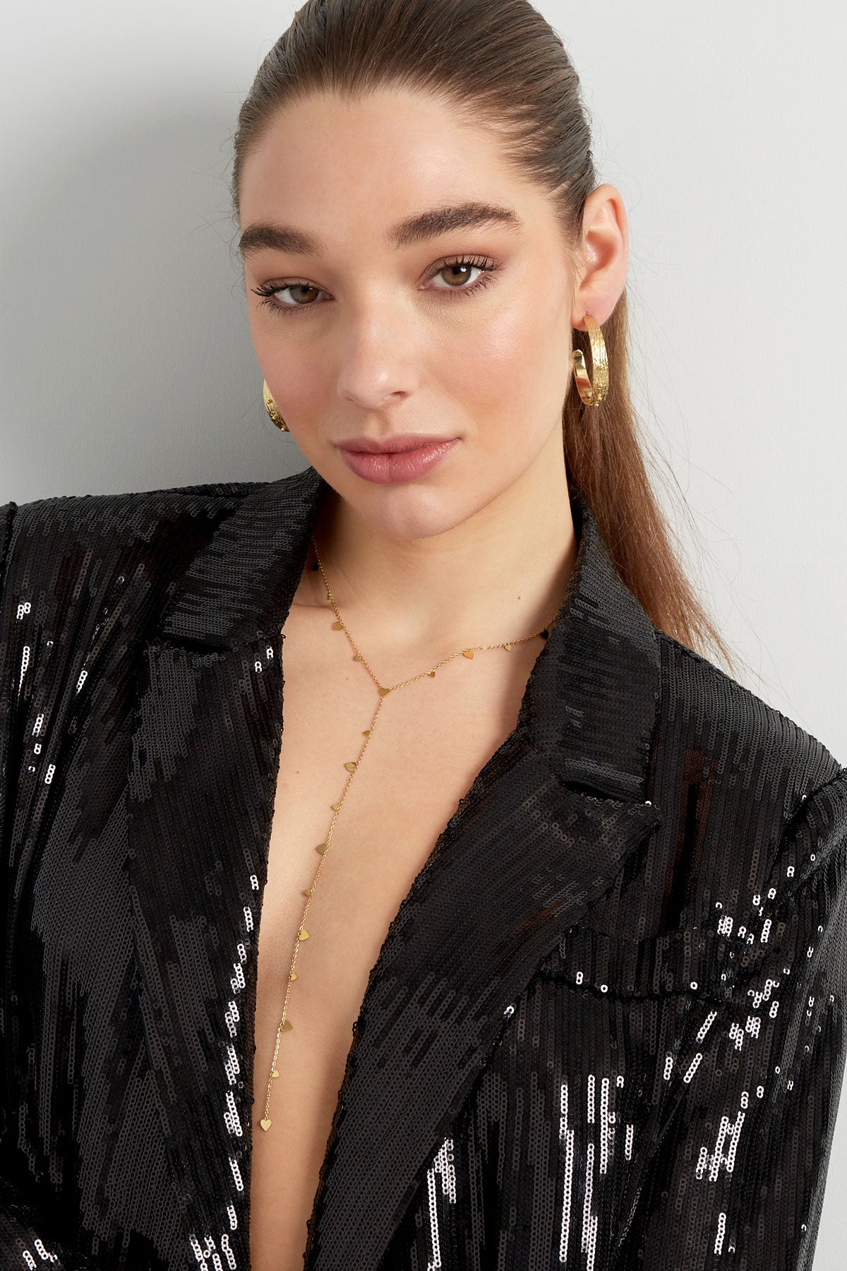 Model wearing gold delicate heart dangle necklace with a black sequin blazer