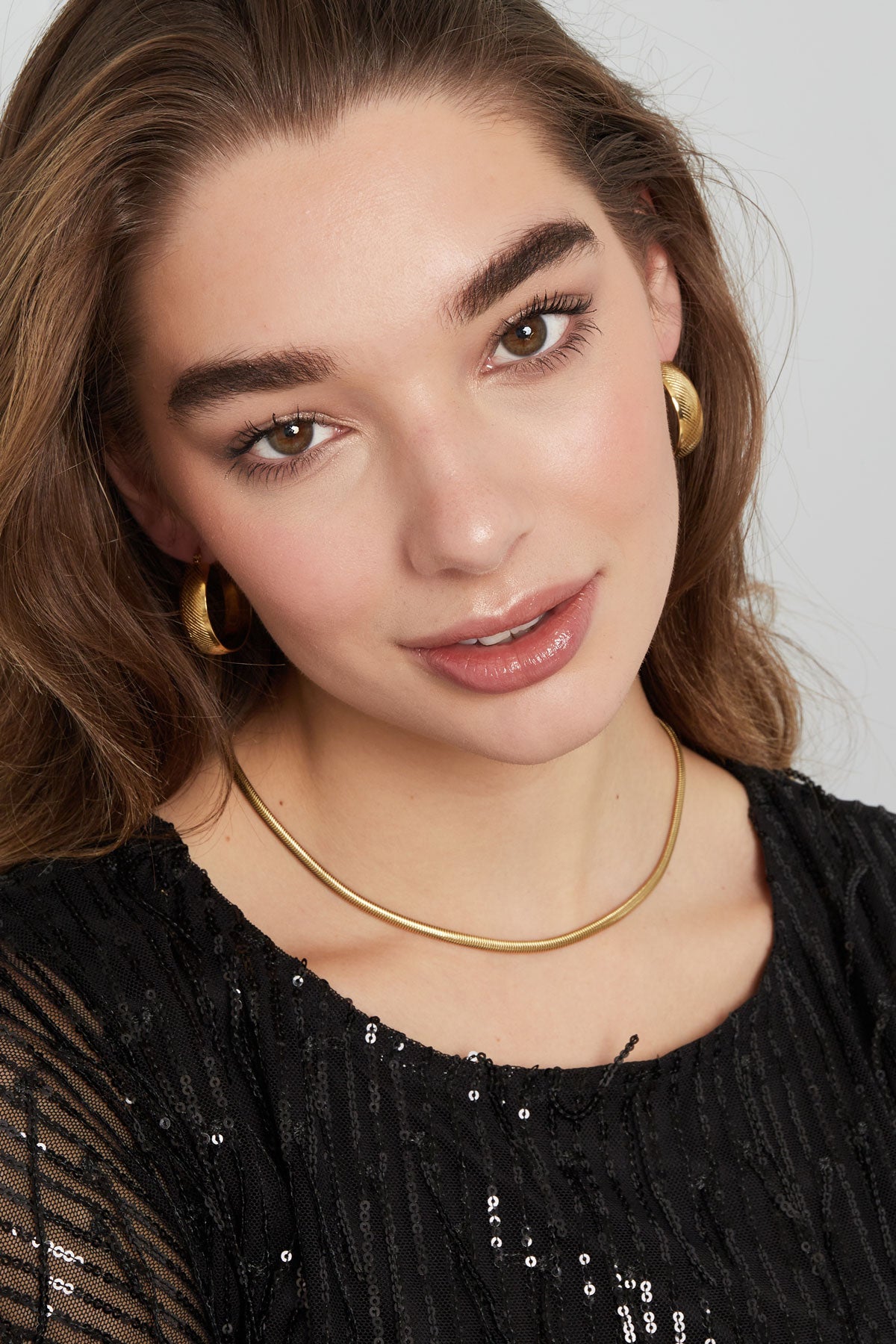 Model portrait with gold snake chain necklace and matching hoop earrings, smiling softly