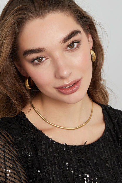 Model portrait with gold snake chain necklace and matching hoop earrings, smiling softly