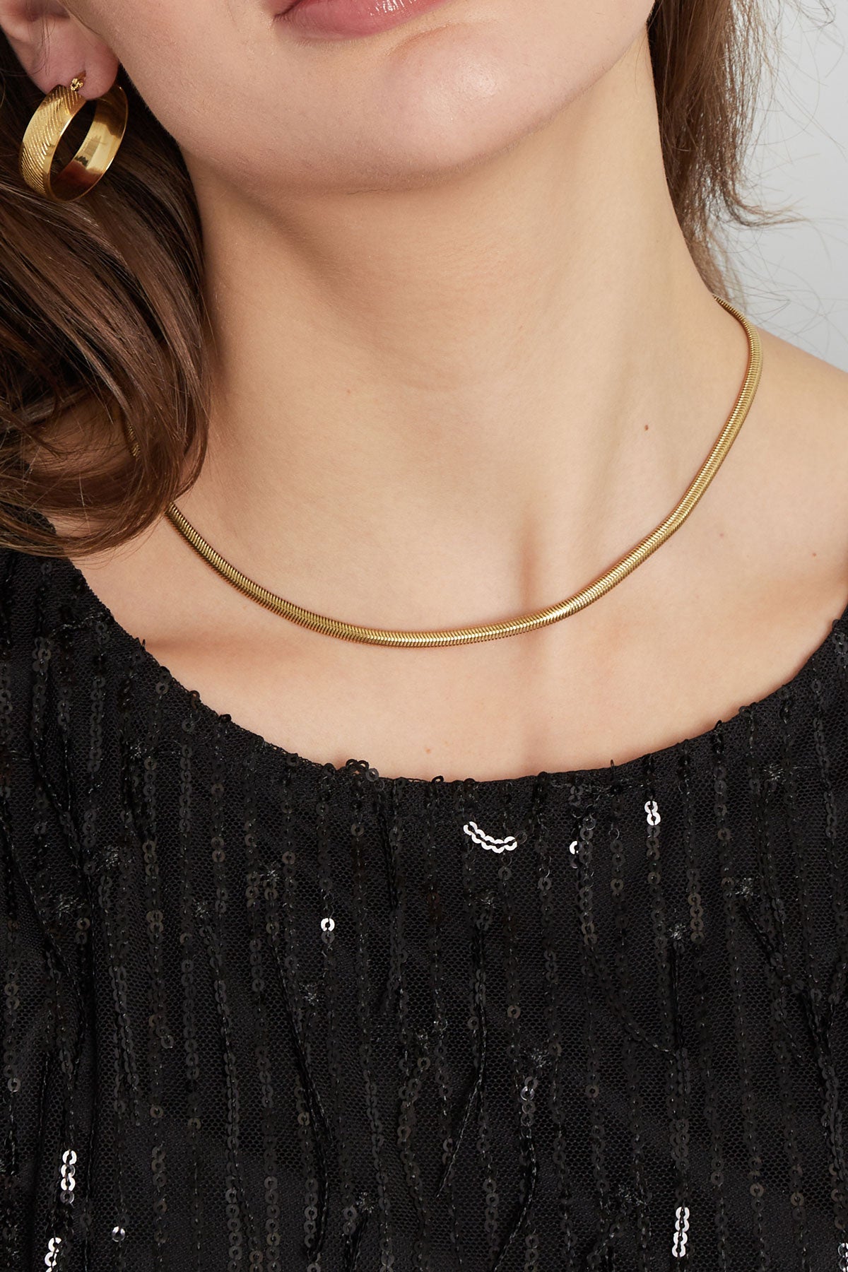 Close-up of gold snake chain necklace on model wearing shimmering black top