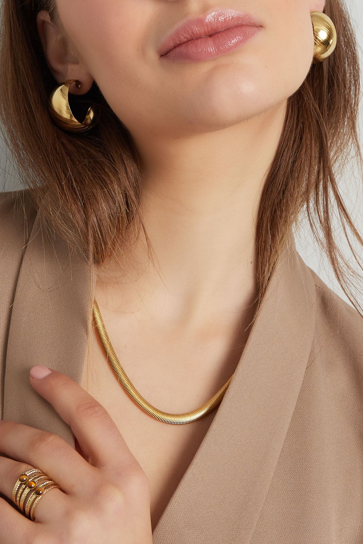 Close-up view of the model’s neckline showcasing the gold flat chain necklace and textured gold rings and earrings