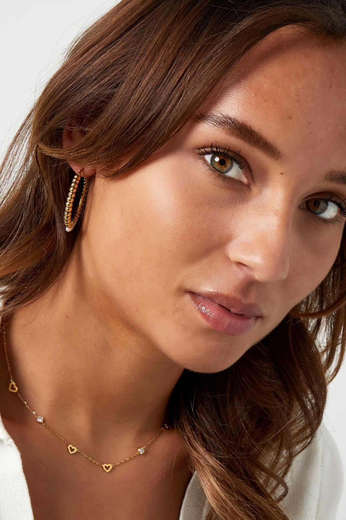 Close-up of a woman wearing the gold heart charm necklace with matching hoop earrings, showing youthful aesthetic style