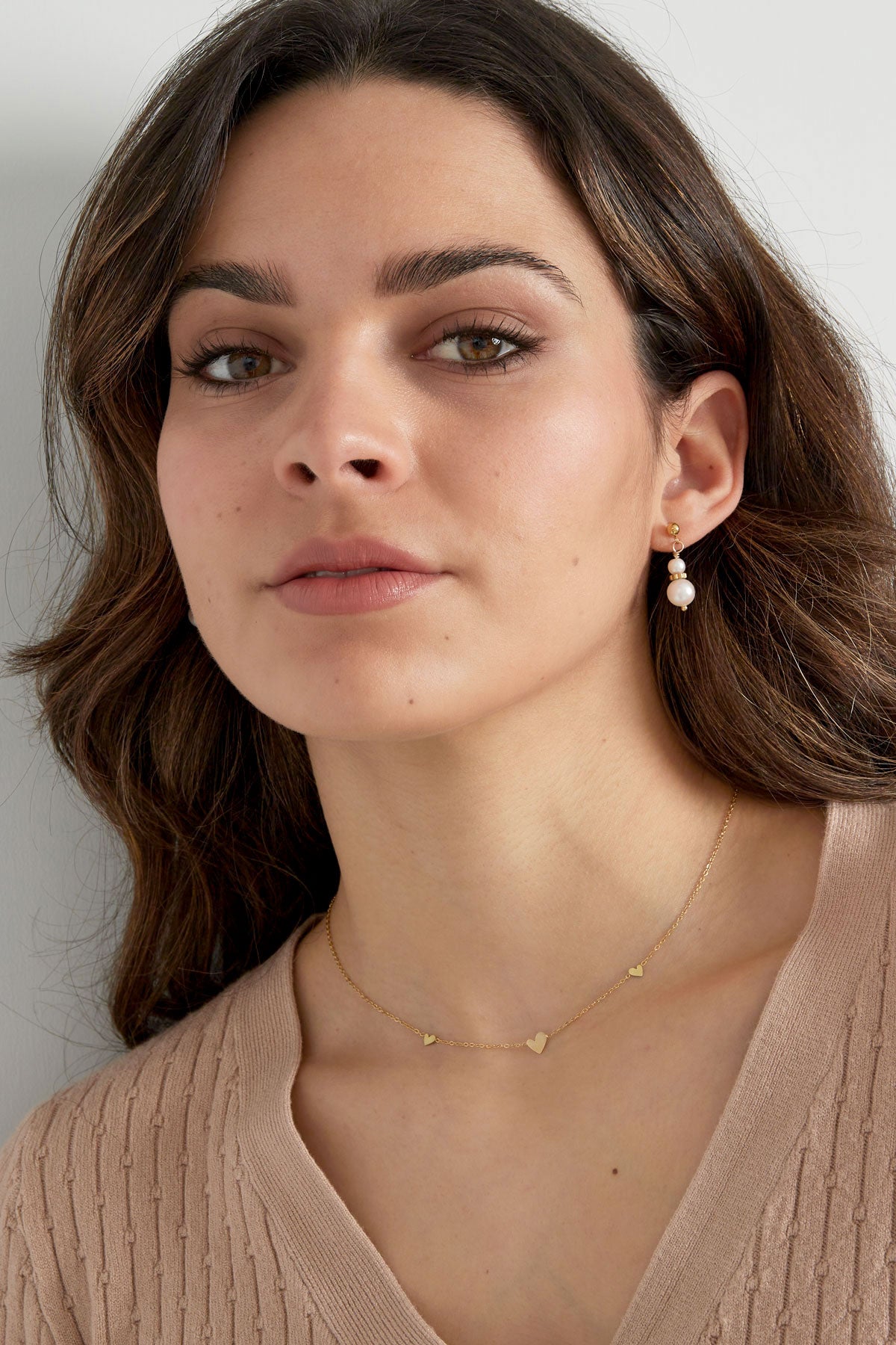 Model wearing gold heart charm necklace and pearl drop earrings