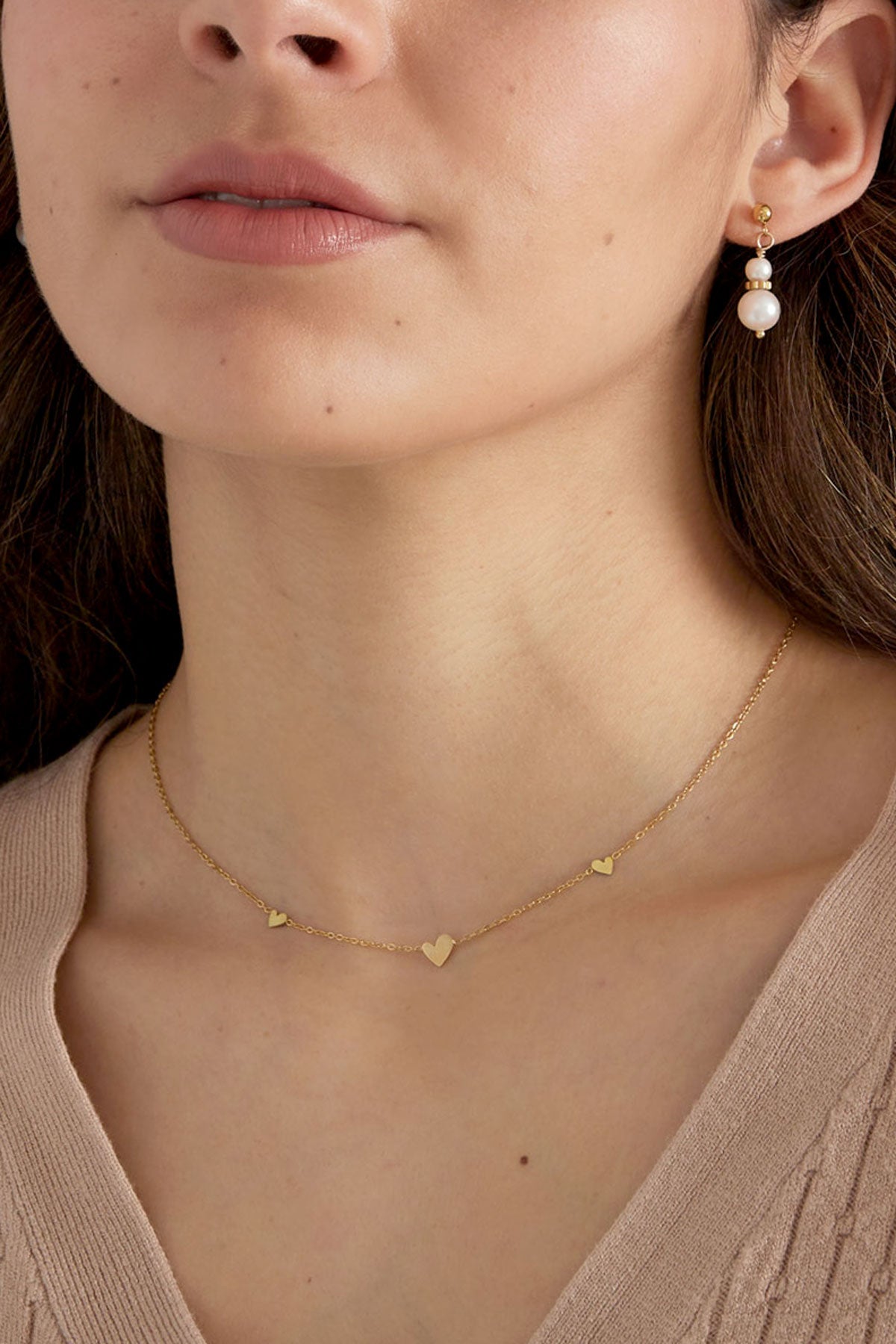 Close-up of model's neck showing gold heart charm necklace and pearl earrings