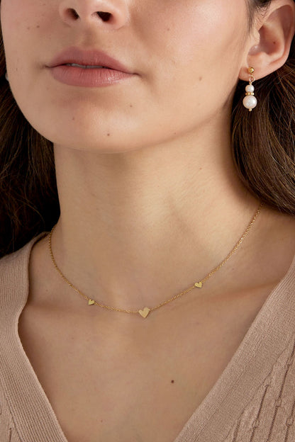 Close-up of model's neck showing gold heart charm necklace and pearl earrings