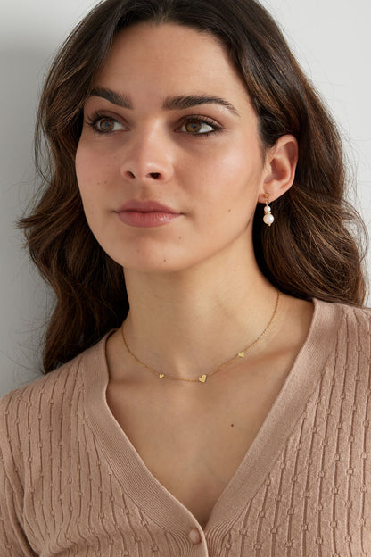 Close-up focused on model's neck with gold heart charm necklace