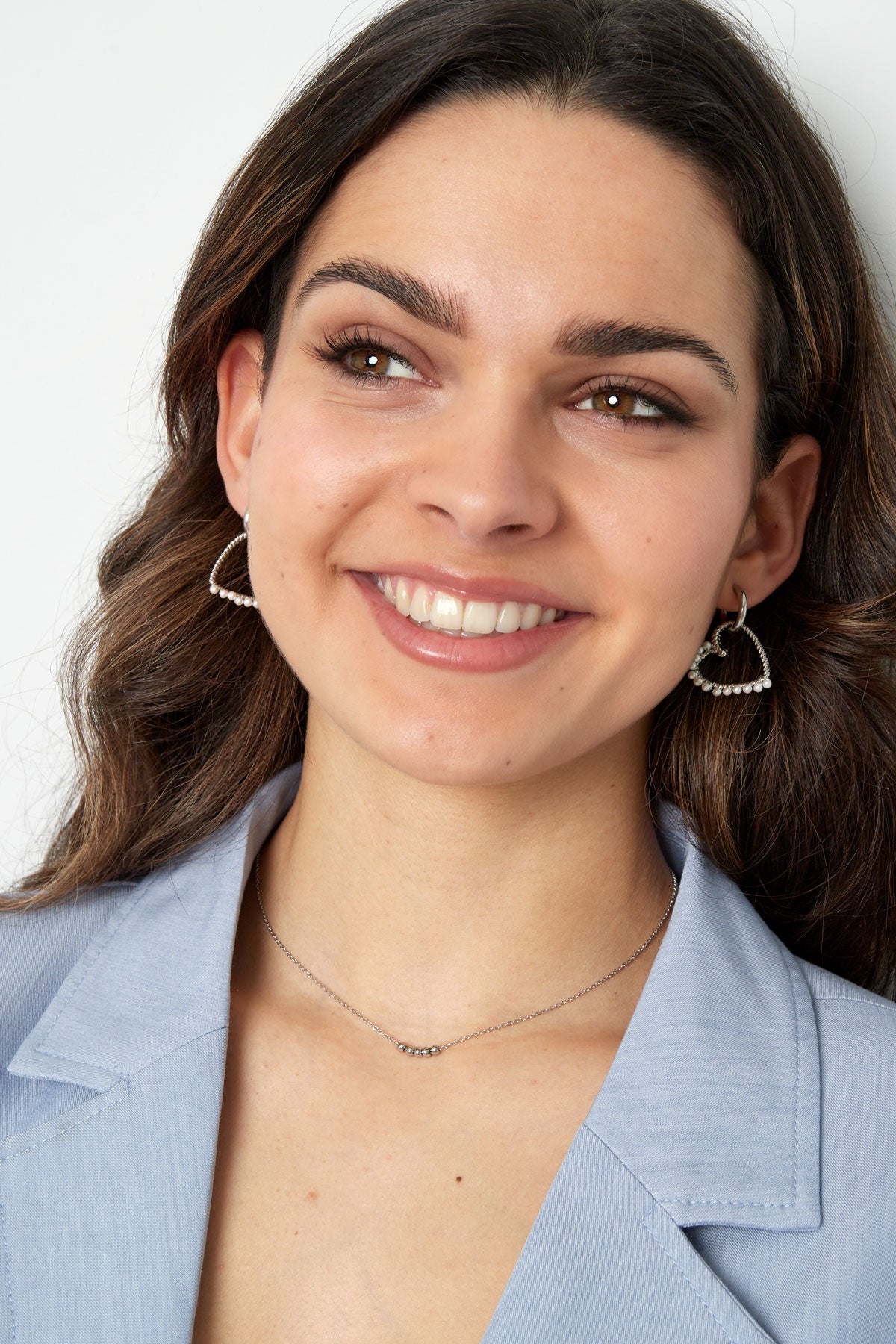 Smiling woman wearing minimalist silver ball chain necklace and heart-shaped pearl earrings