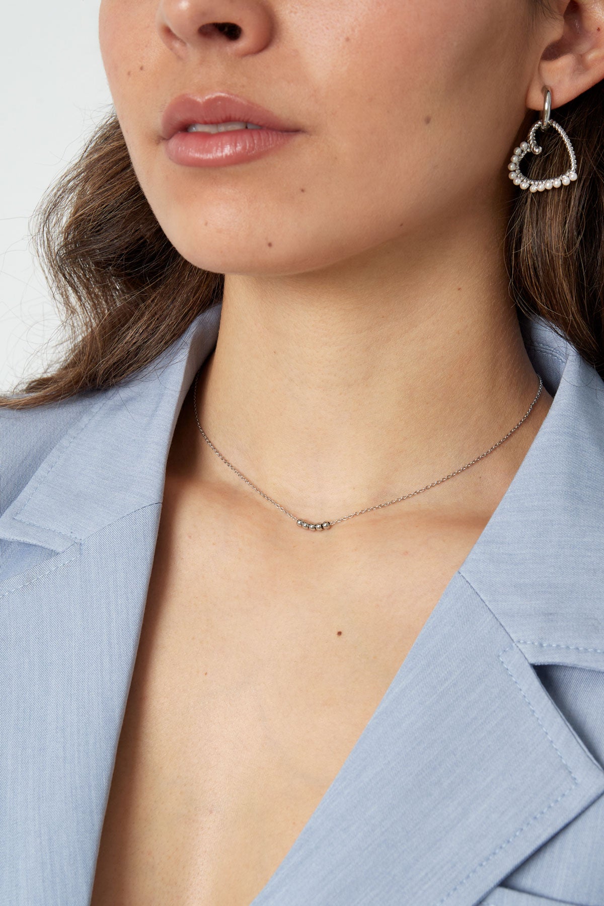 Side profile of woman showcasing silver ball chain necklace paired with heart-shaped pearl earrings