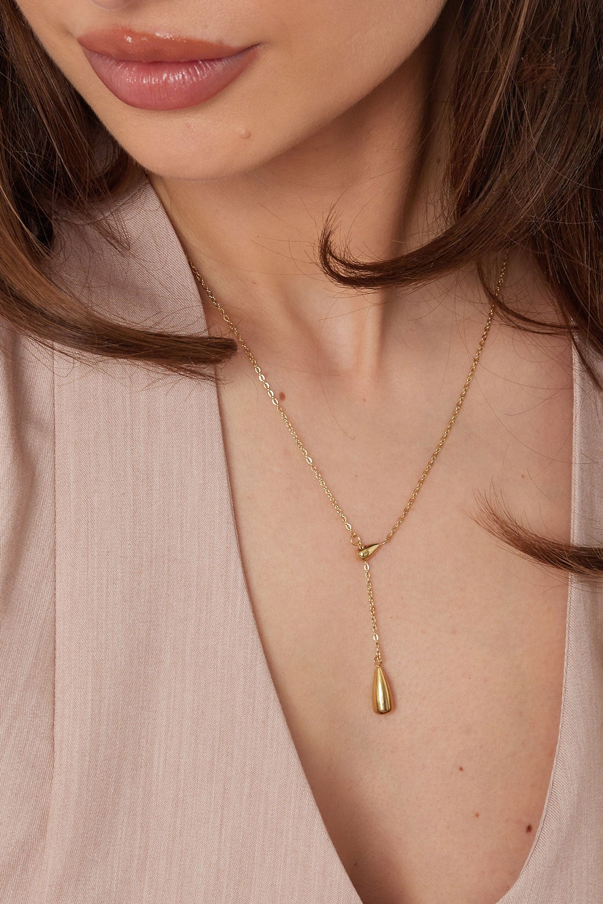 Close-up of woman wearing gold drop charm necklace highlighting the pendant detail