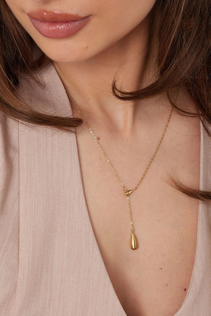 Close-up of woman wearing gold drop charm necklace highlighting the pendant detail