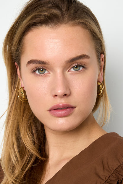 Model wearing Petit Coeur gold hoops, featuring delicate heart-shaped accents on a slender circular frame.