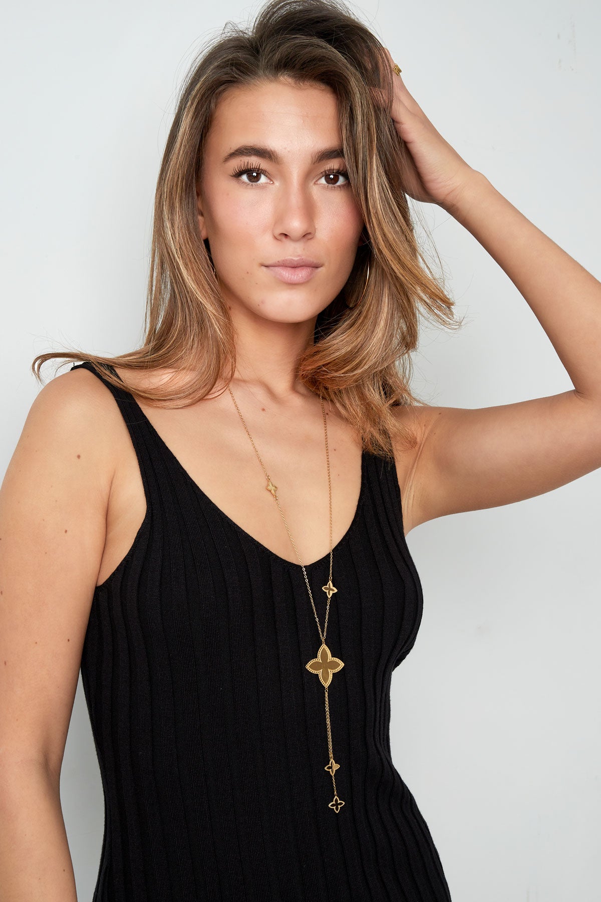 Model wearing gold clover charm necklace paired with black sleeveless top, showcasing length and charm details