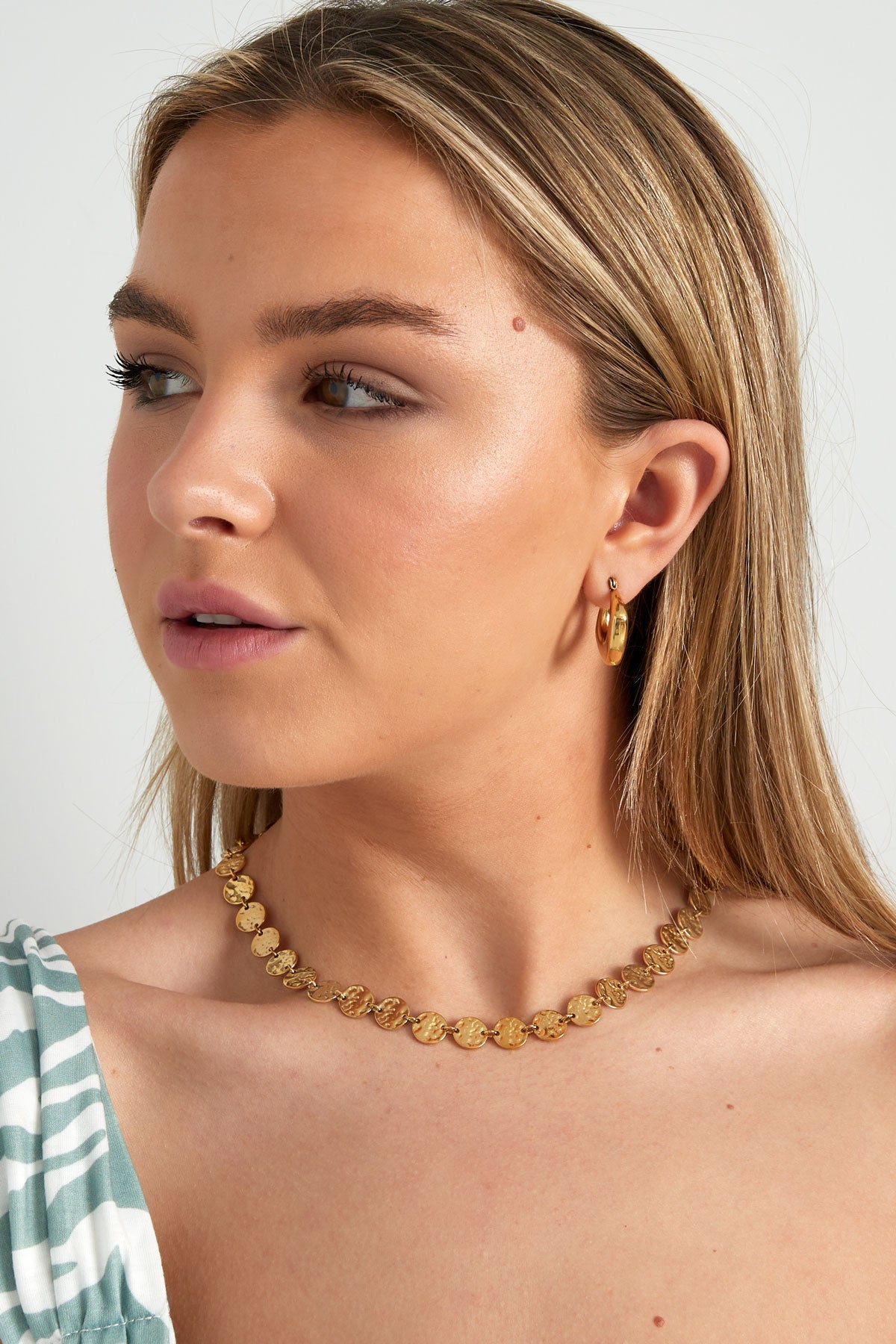 Woman wearing hammered gold disc necklace and gold hoop earrings, styled with a striped top