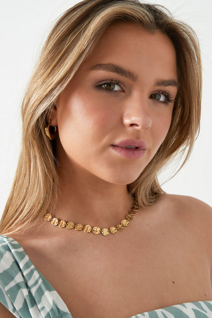 Model wearing the hammered gold disc necklace paired with gold hoop earrings and a striped off-shoulder top