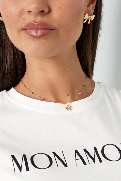 Detailed view of a woman wearing the gold bow pendant necklace paired with a white t-shirt printed with 'MON AMOUR'