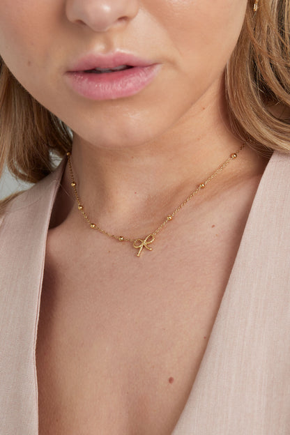 Model wearing a gold bow pendant necklace, showcasing the necklace resting comfortably around the neck with a soft, youthful look
