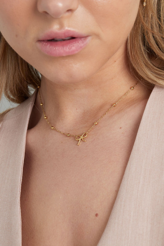 Model wearing a gold bow pendant necklace, showcasing the necklace resting comfortably around the neck with a soft, youthful look