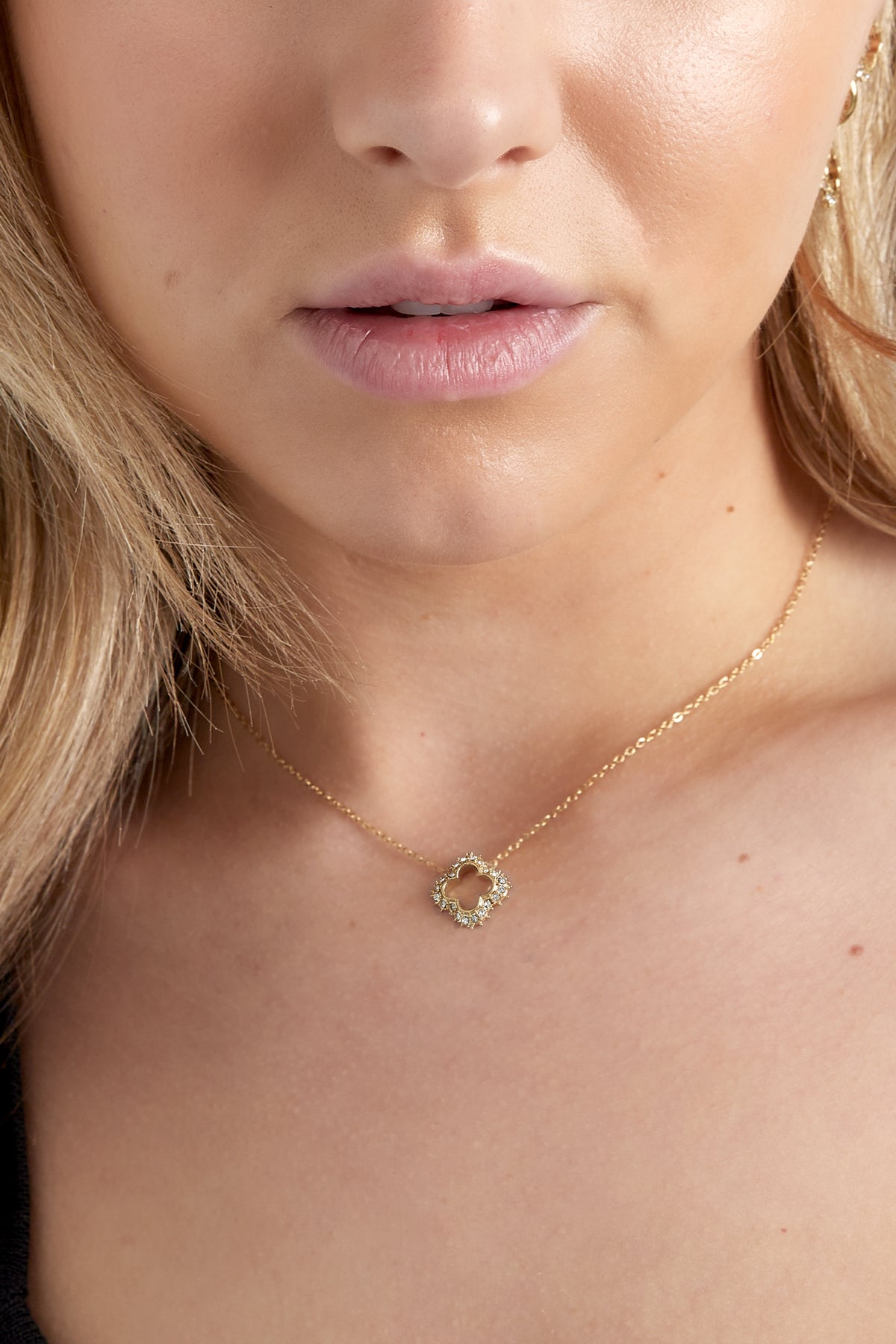 Woman wearing gold clover pendant necklace showcasing its elegant sparkle near her collarbone