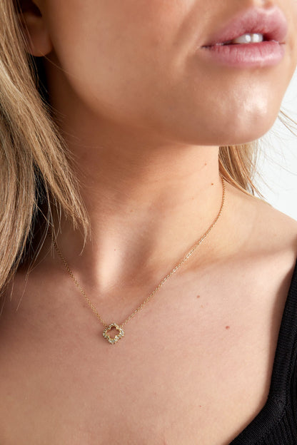 Side view of woman in black top wearing the gold clover pendant necklace with a soft, aesthetic look