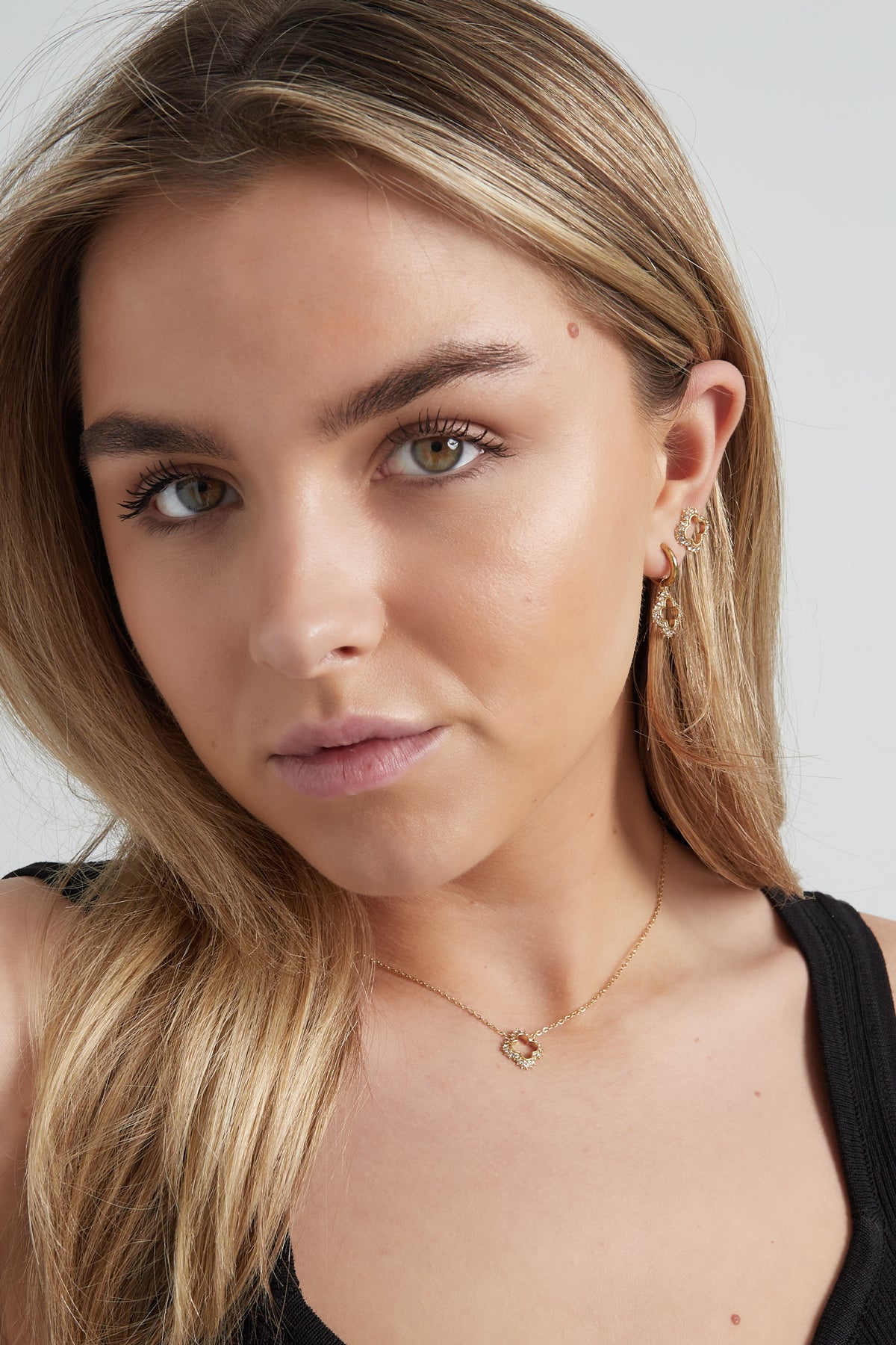 Portrait of woman wearing matching gold clover pendant necklace and earrings in a boutique style