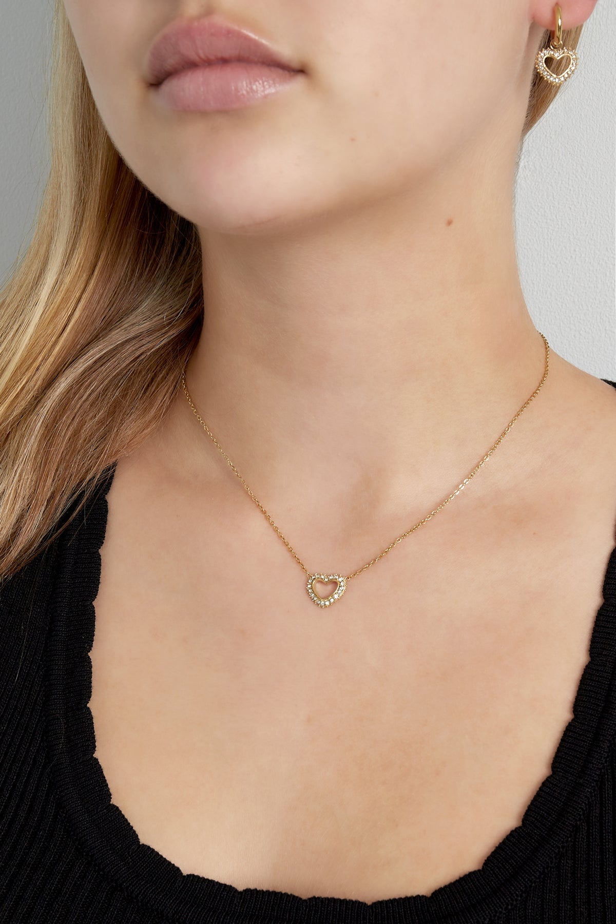 Close-up of woman wearing the gold heart pendant necklace and matching heart earrings with crystal details