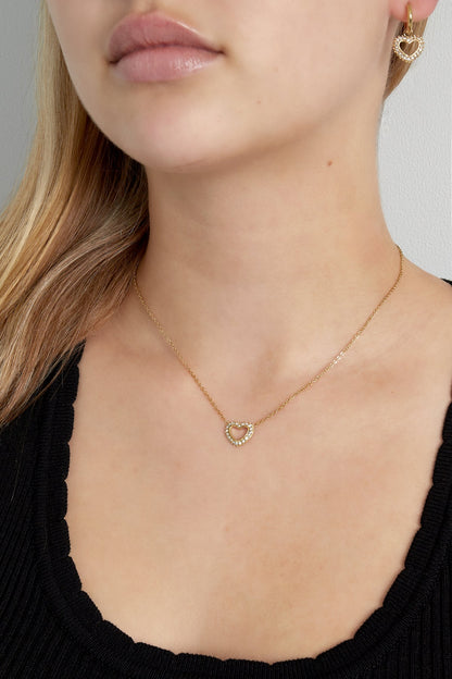 Close-up of woman wearing the gold heart pendant necklace and matching heart earrings with crystal details