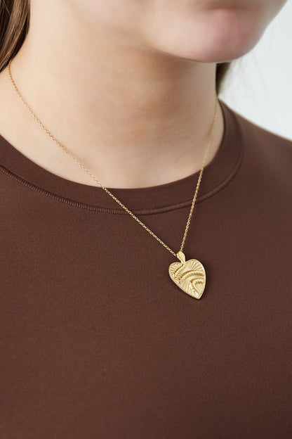 Close-up of a woman wearing gold textured heart pendant necklace paired with chocolate brown top