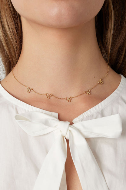 Close-up of a woman wearing the gold bow necklace paired with a white top with bow detail