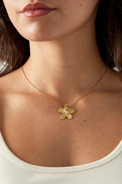 Close-up of a woman wearing a gold flower necklace with pearl detail against bare skin and a white top