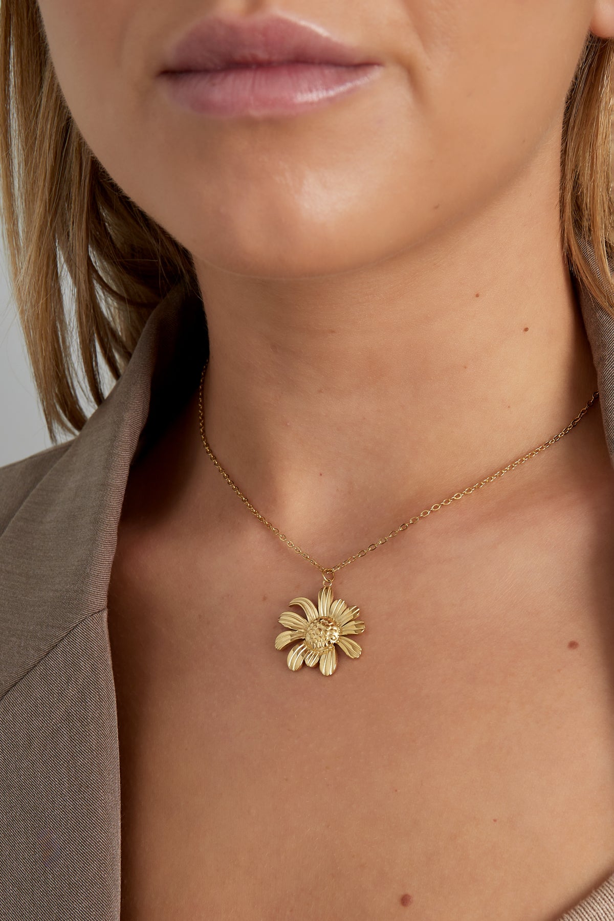 Model wearing the golden daisy pendant necklace close to the neck, showing natural skin tone and soft lighting