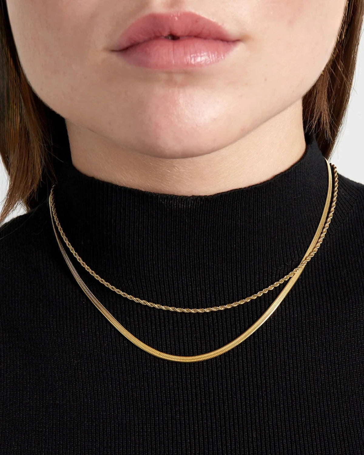 Two gold chain necklaces worn on a person wearing a black top.