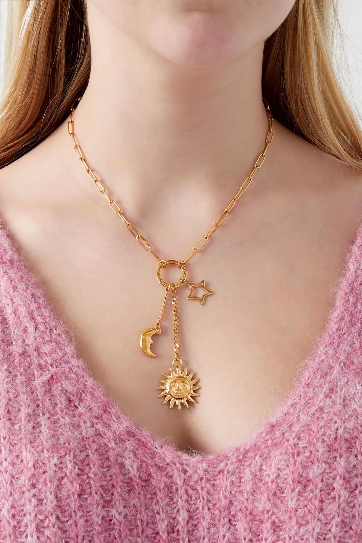 Close-up of woman wearing gold celestial charm necklace with sun, moon and star pendants paired with pink fluffy knit top