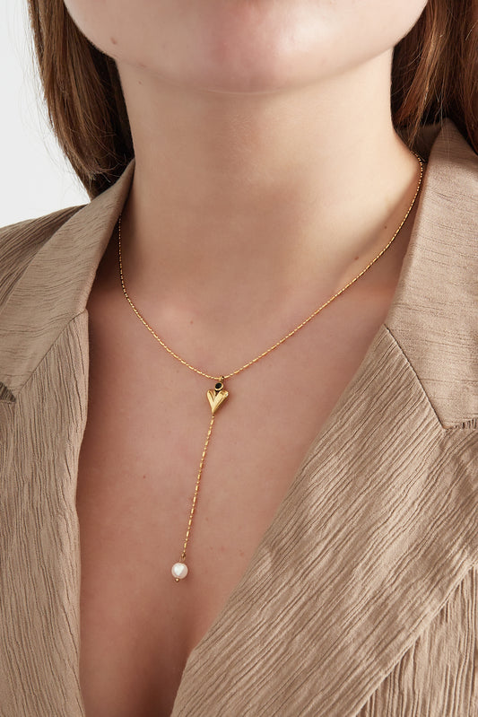Close-up of model wearing delicate gold heart pearl necklace with beige textured blazer