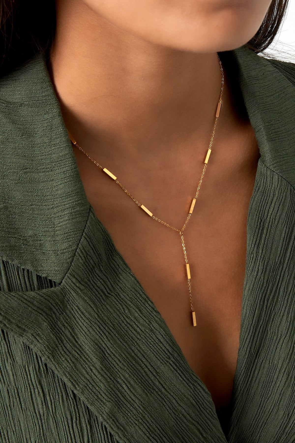 Close-up of woman wearing the gold-tone modern bar pendant necklace paired with a green textured blouse