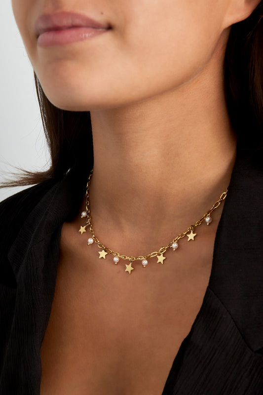 Close-up of a woman wearing a gold-tone star charm and pearl necklace paired with a black top